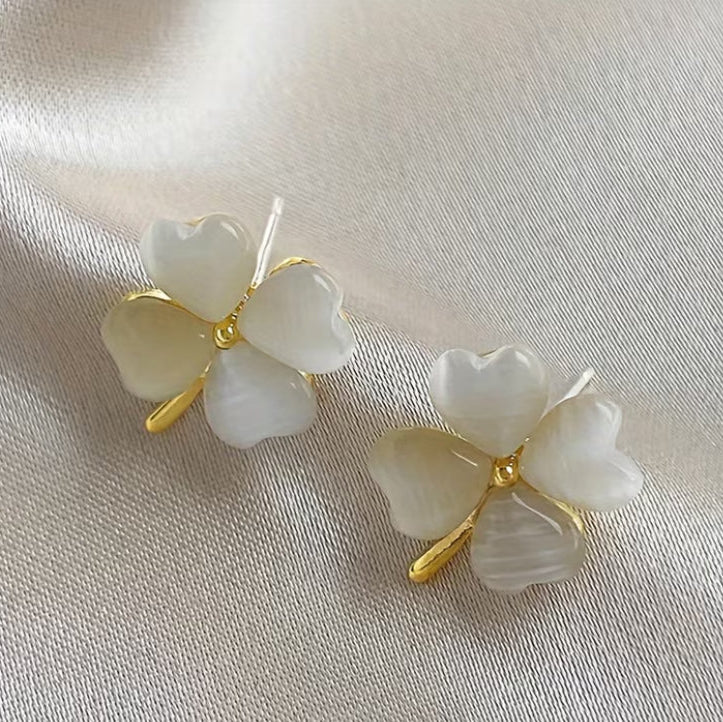 Pair of white Opalescent Clover Earrings with gold accents on a light fabric background