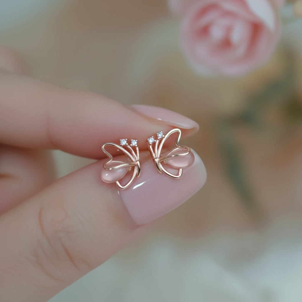 Rose Gold Butterfly Pearl Earrings on a finger with a blurred background