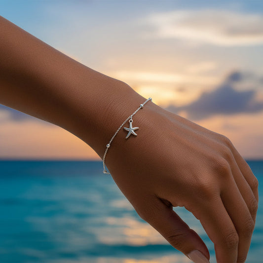 Hand wearing a silver Coastal Starfish Bead Bracelet with a sunset and ocean background