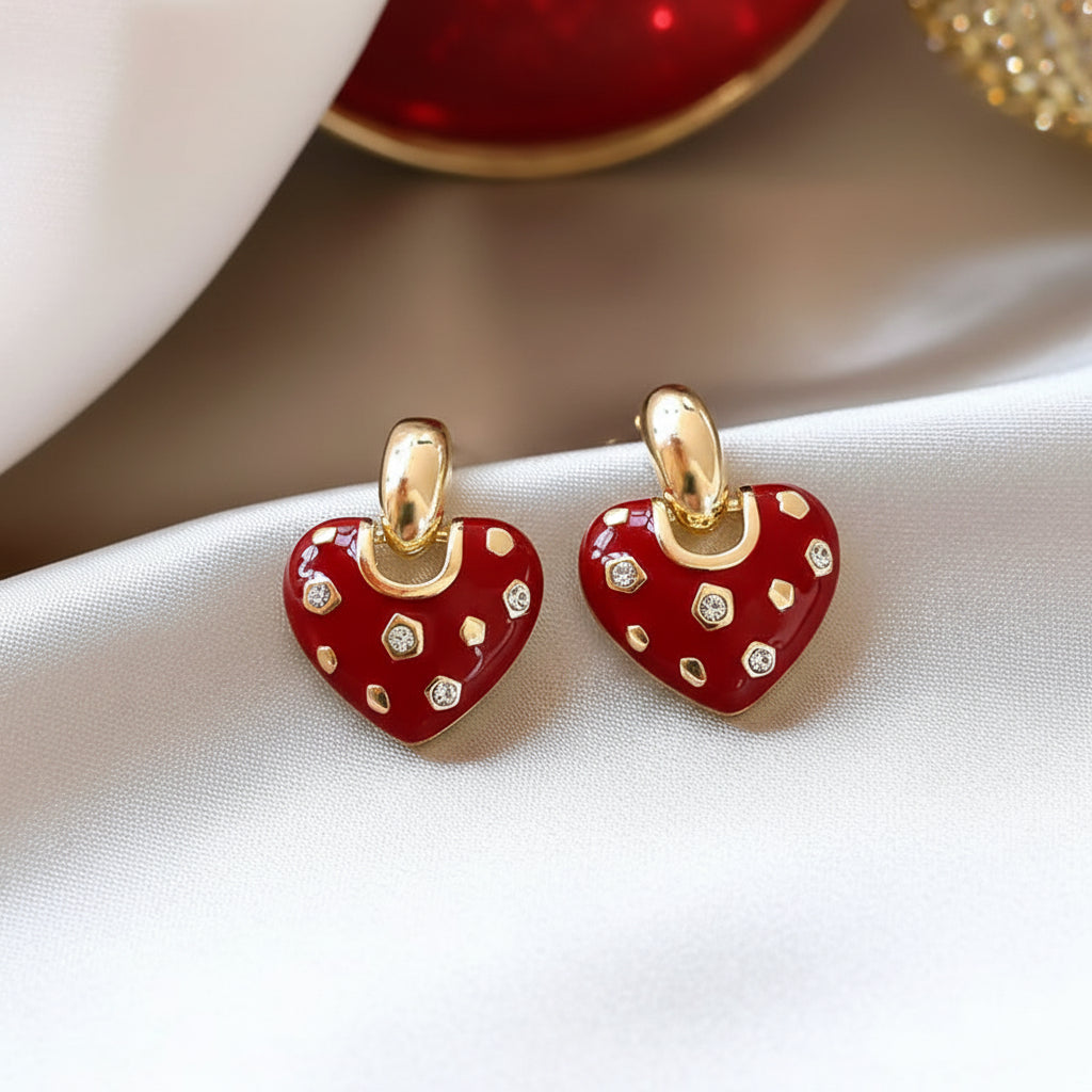 Crystal Accent Red Heart Earrings with red enamel and gold accents on a beige fabric background