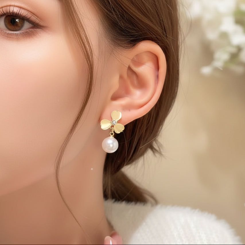 Close-up of an ear wearing a Luminous Gold Clover Pearl Drop Earrings against a neutral background