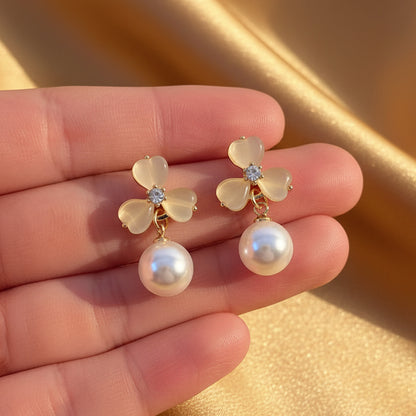 Luminous Gold Clover Pearl Drop Earrings with pearls held between fingers against a white fabric background