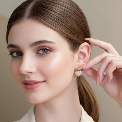 Close-up of a person wearing Gold Pearl Blossom Hoop Earrings, holding one earring with a blurred background.
