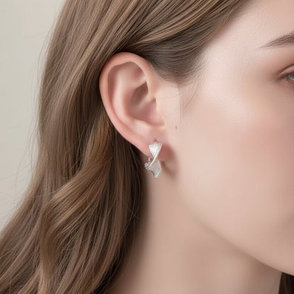 Silver Woven Twist Hoop Earrings being held near an ear with a neutral background