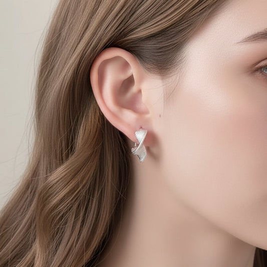 Silver Woven Twist Hoop Earrings being held near an ear with a neutral background