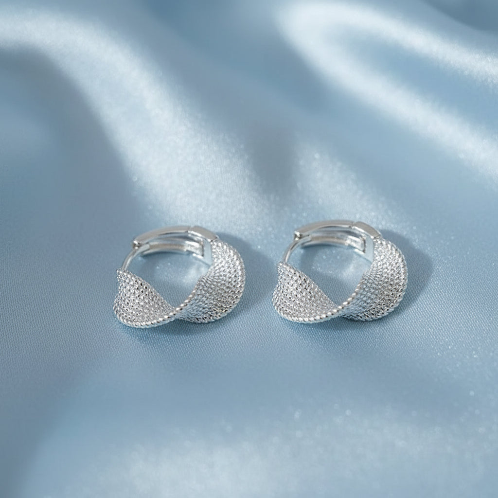 Silver Woven Twist Hoop Earrings on a beige fabric background with a card.