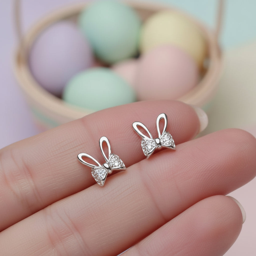 Silver Sparkle Bunny Bow Earrings held between fingers with pastel-colored eggs in the background
