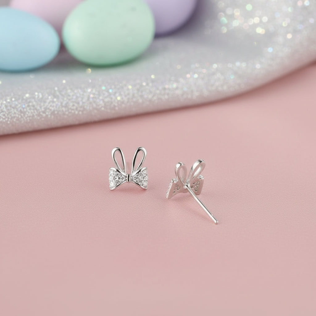 Silver Sparkle Bunny Bow Earrings on a pink surface with colorful eggs in the background
