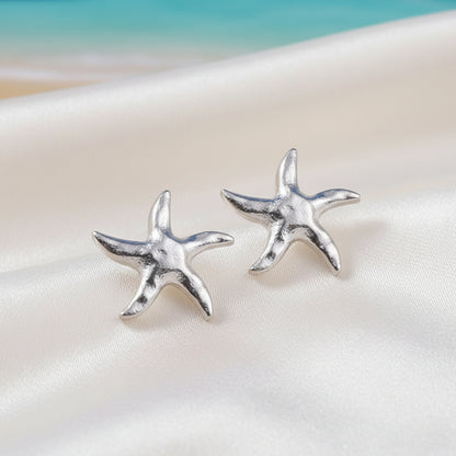 Silver Tide Starfish Earrings on a white surface with a blurred background