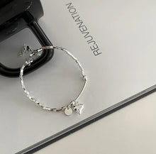 Load image into Gallery viewer, Close-up of the heart charm and bead detail on the sterling silver bracelet, highlighting its elegant design, on white paper with black.