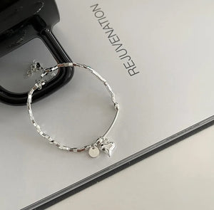 Close-up of the heart charm and bead detail on the sterling silver bracelet, highlighting its elegant design, on white paper with black.