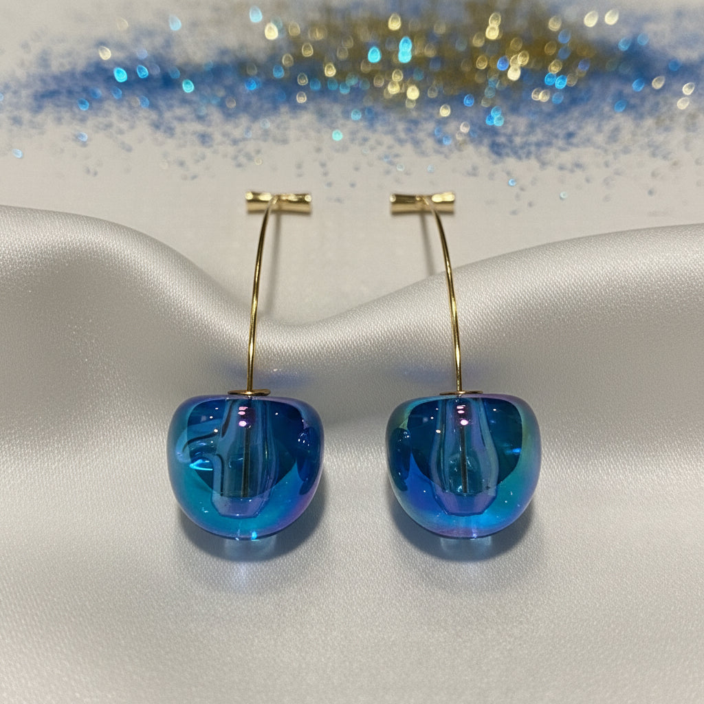 Iridescent Blue Cherry Drop Earrings with gold hooks on a silver surface