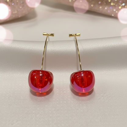 Iridescent Red Cherry Drop Earrings with gold hooks on a light pink background