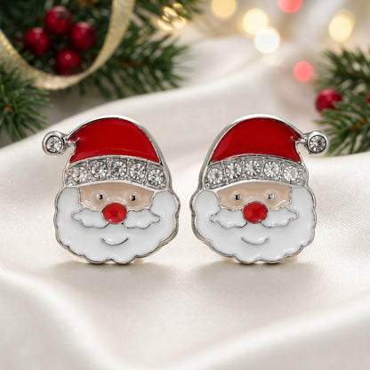 A pair of Jolly Santa Earrings with red enamel hats, white enamel beard, and clear rhinestone trim, set in silver-tone metal on a warm beige background.
