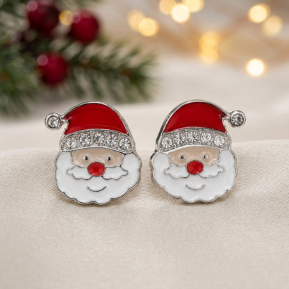 A pair of Jolly Santa Earrings with red enamel hats, white enamel beard, and clear rhinestone trim, set in silver-tone metal on a warm beige background.