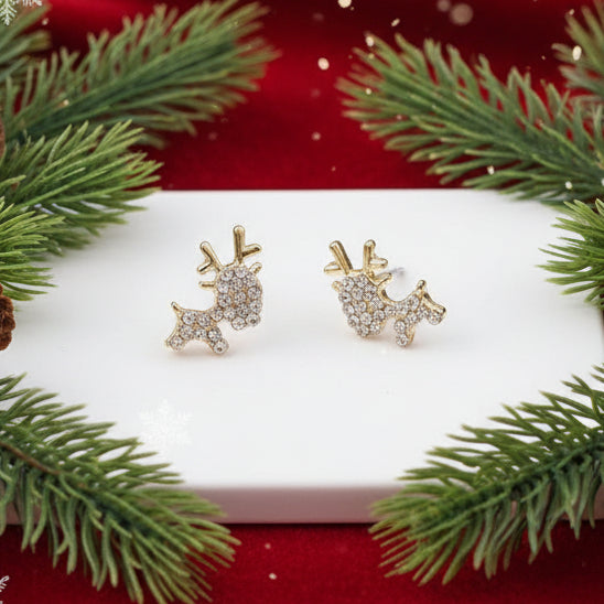 Gold Zircon Reindeer Earrings on a white surface with a gold ring and green leaves in the background.