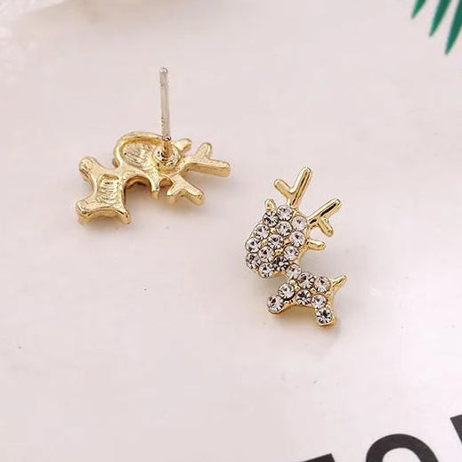 Gold Zircon Reindeer Earrings on a white surface with green leaves in the background