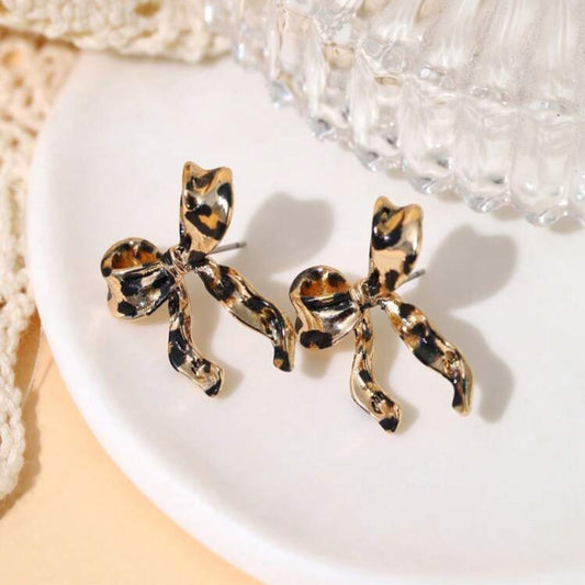 Leopard print bow-shaped earrings on a white plate with a textured background