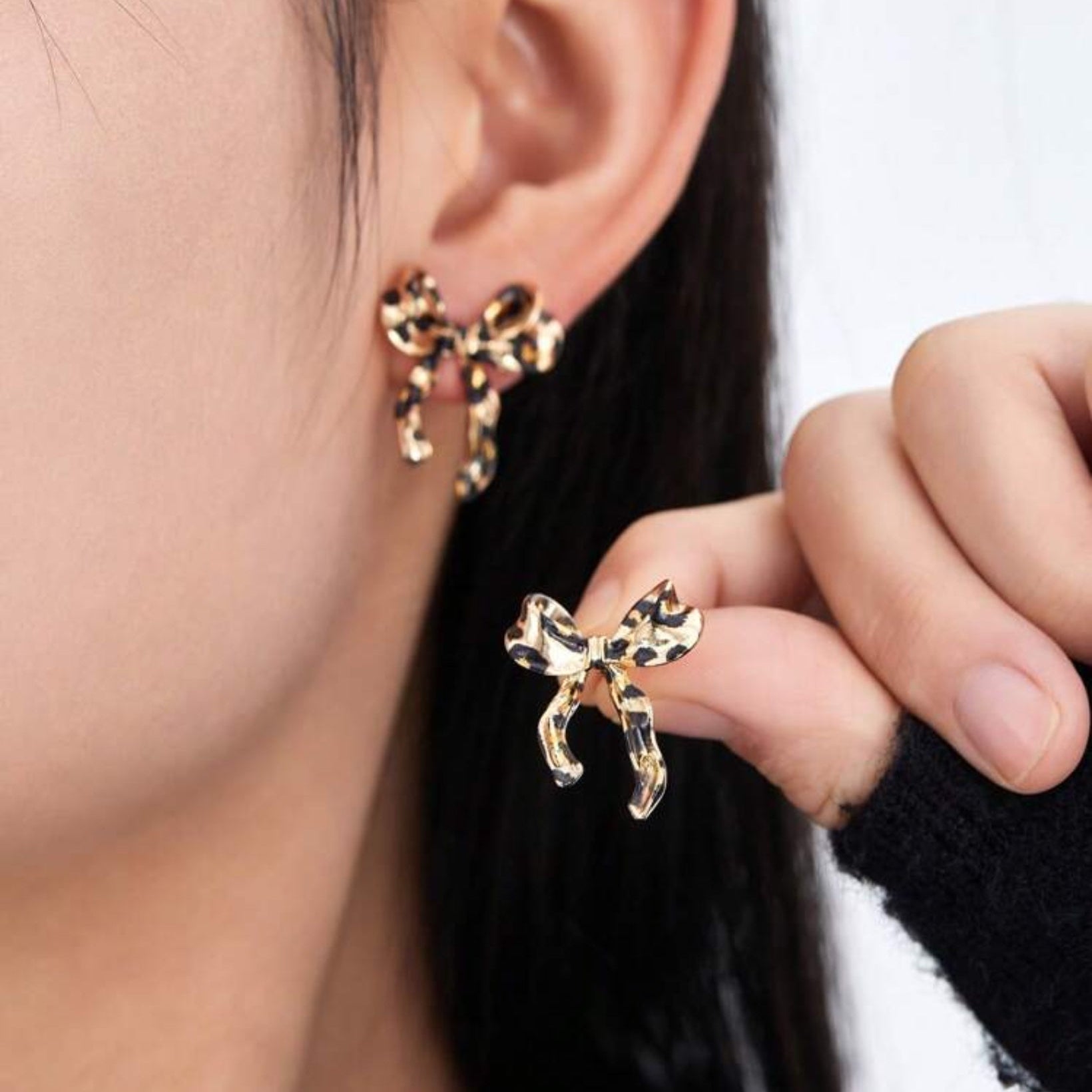 Leopard print bow-shaped earrings worn by a person.