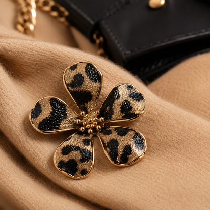 A Leopard Print Flower Pin with a black and tan leopard print pattern, resting on a beige coat next to a black leather handbag.