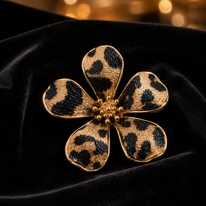 A Leopard Print Flower Pin with a leopard print pattern in black and tan, accented with a gold beaded center, displayed on a black velvet surface.