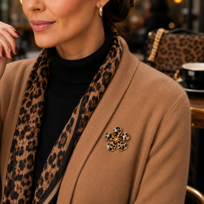 A close-up lifestyle shot of a woman wearing a Leopard Print Flower Pin, pinned to her tan blazer over a black turtleneck and a leopard print scarf.
