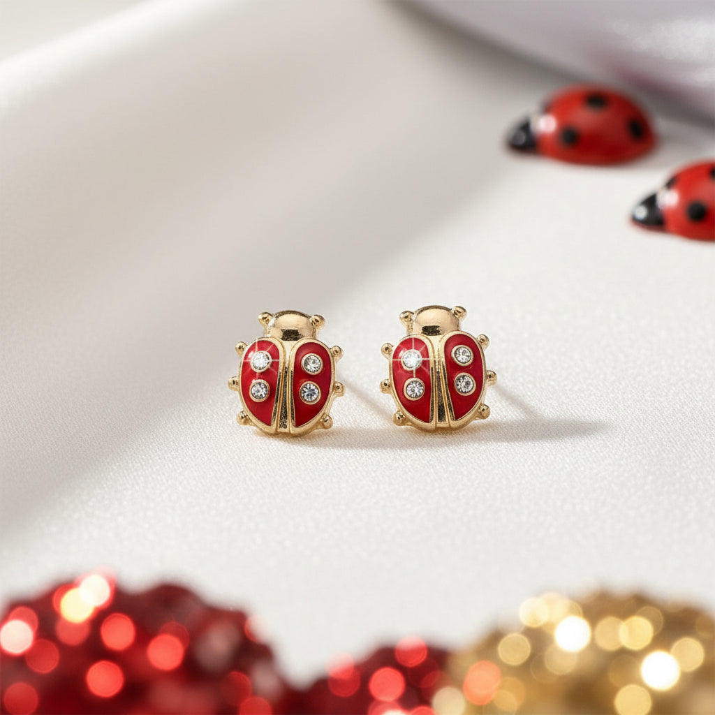 Red and gold Little Lucky Ladybug Earrings on a white surface with blurred red and gold objects in the foreground.