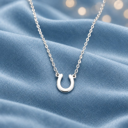 A silver Lucky Horseshoe Necklace, displayed against a draped light blue satin fabric background.