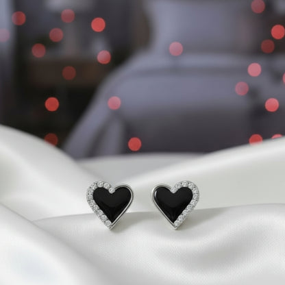 Midnight Black Heart Rhinestone Earrings on a white surface with red and pink bokeh lights in the background.