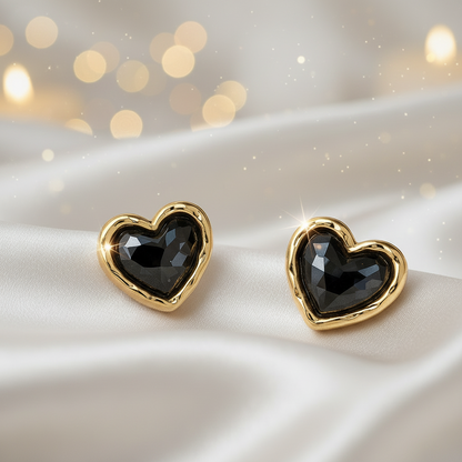 Midnight Mosaic Black & Gold Heart Earrings on a satin surface with blurred lights in the background.