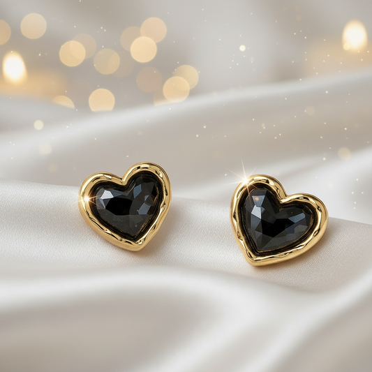 Midnight Mosaic Black & Gold Heart Earrings on a satin surface with blurred lights in the background.