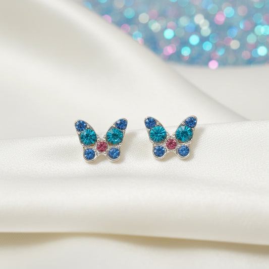 Mini Blue Crystal Butterfly Earrings with colorful gemstones on a white surface with a glittery blue background.