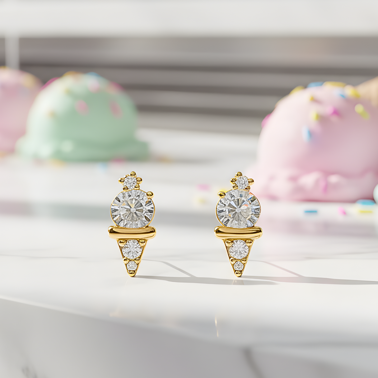 Mini Gold Ice Cream CZ Earrings with clear gemstones on a white surface with colorful pastries in the background