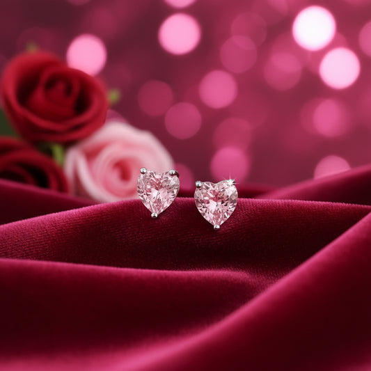 Mini Pink Crystal Heart Earrings on a red fabric with blurred pink flowers in the background