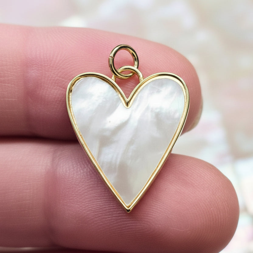 Mother-of-Pearl Heart Charm with gold frame held between fingers against a blurred background