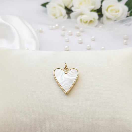 Mother-of-Pearl Heart Charm with gold border on a white cushion with flowers and pearls in the background