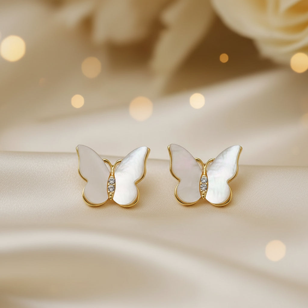 Mother of Pearl Butterfly Earrings with gold accents on a beige surface
