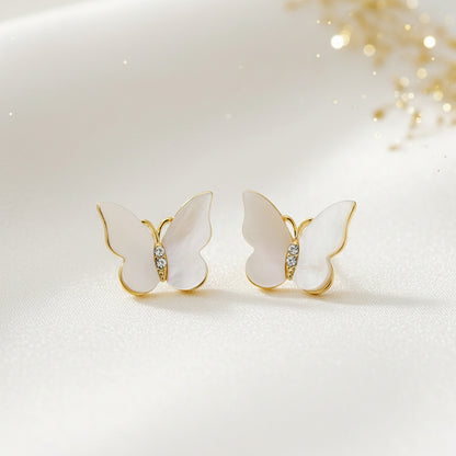 Mother of Pearl Butterfly Earrings with gold and white details on a textured fabric background