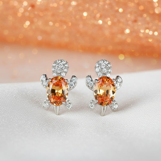 Orange Glow Crystal Turtle Earrings with orange gemstones on a glittery surface