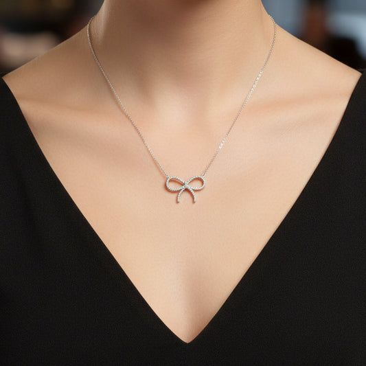 A close-up of a model wearing a Pavé Bow Necklace on a fine chain, paired with a black V-neck top against a softly blurred background.