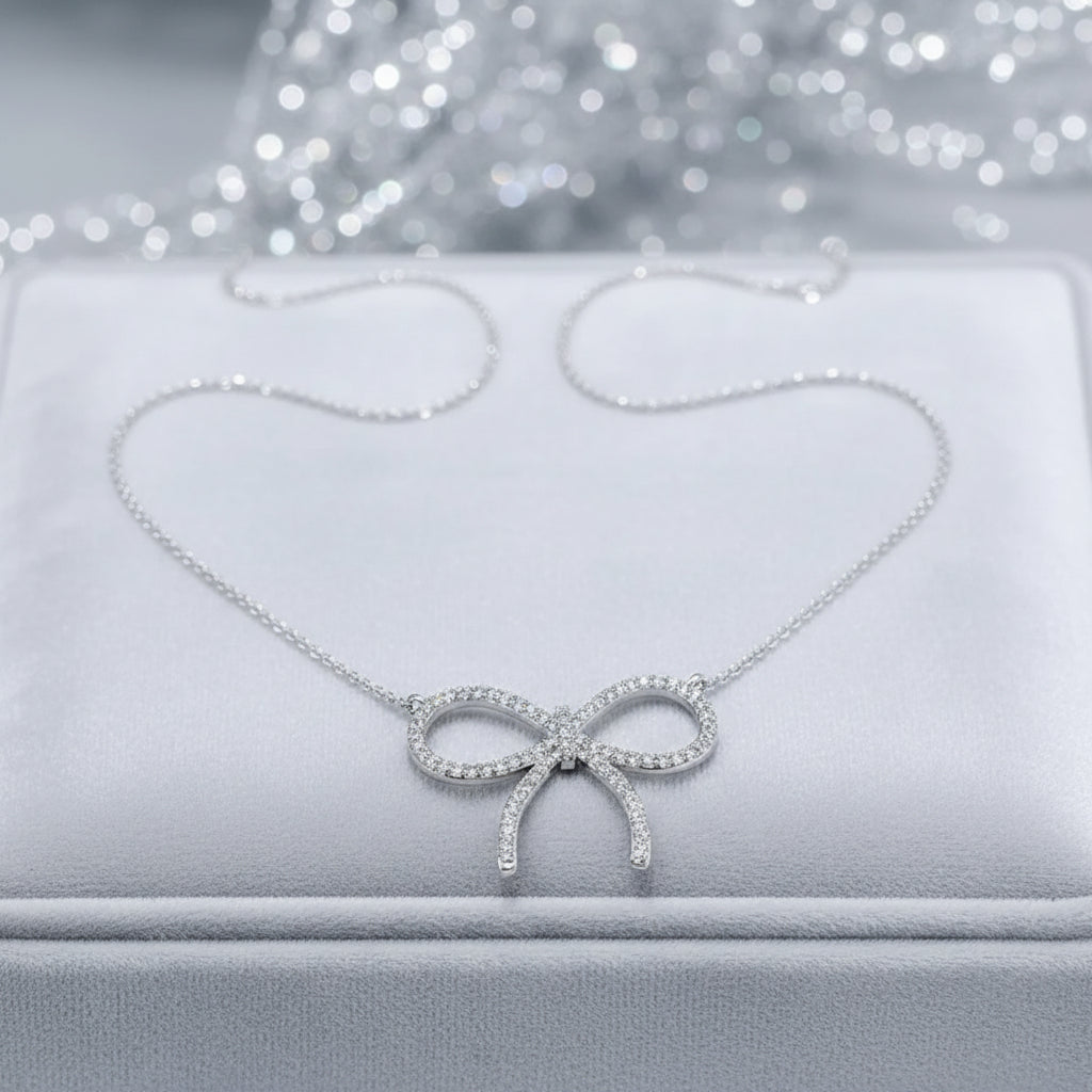 A delicate Pavé Bow Necklace, displayed on a white jewelry box with a sparkling silver bokeh background.