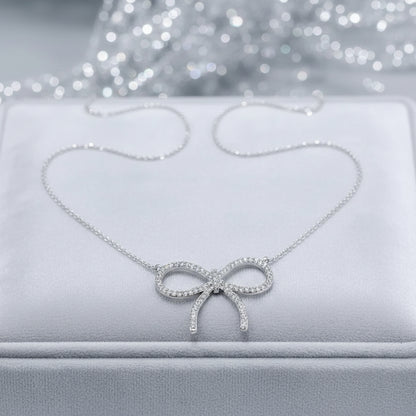 A delicate Pavé Bow Necklace, displayed on a white jewelry box with a sparkling silver bokeh background.