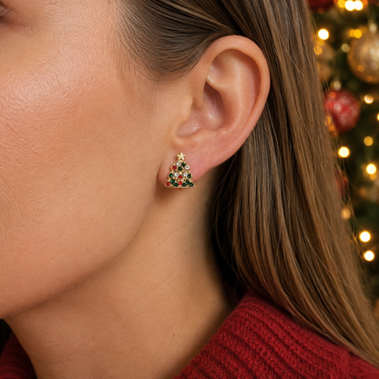 A close-up of a woman's ear wearing a Pavé Christmas Tree Earring with a blurred festive Christmas tree in the background.