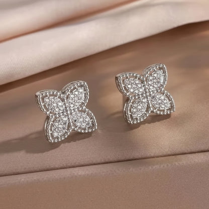 Pavé Crystal Clover Earrings with diamond-like stones on a beige fabric background