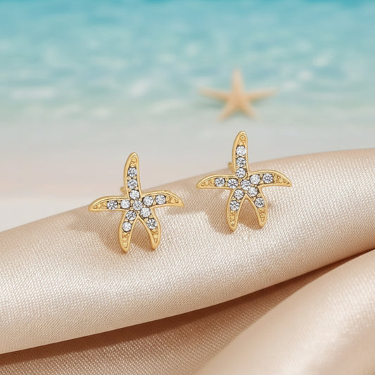 Pavé Starfish Earrings with clear stones on a beige fabric background