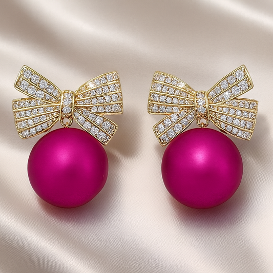 Pink Ornament Pavé Bow Earrings with pink balls and gold bow designs on a satin background