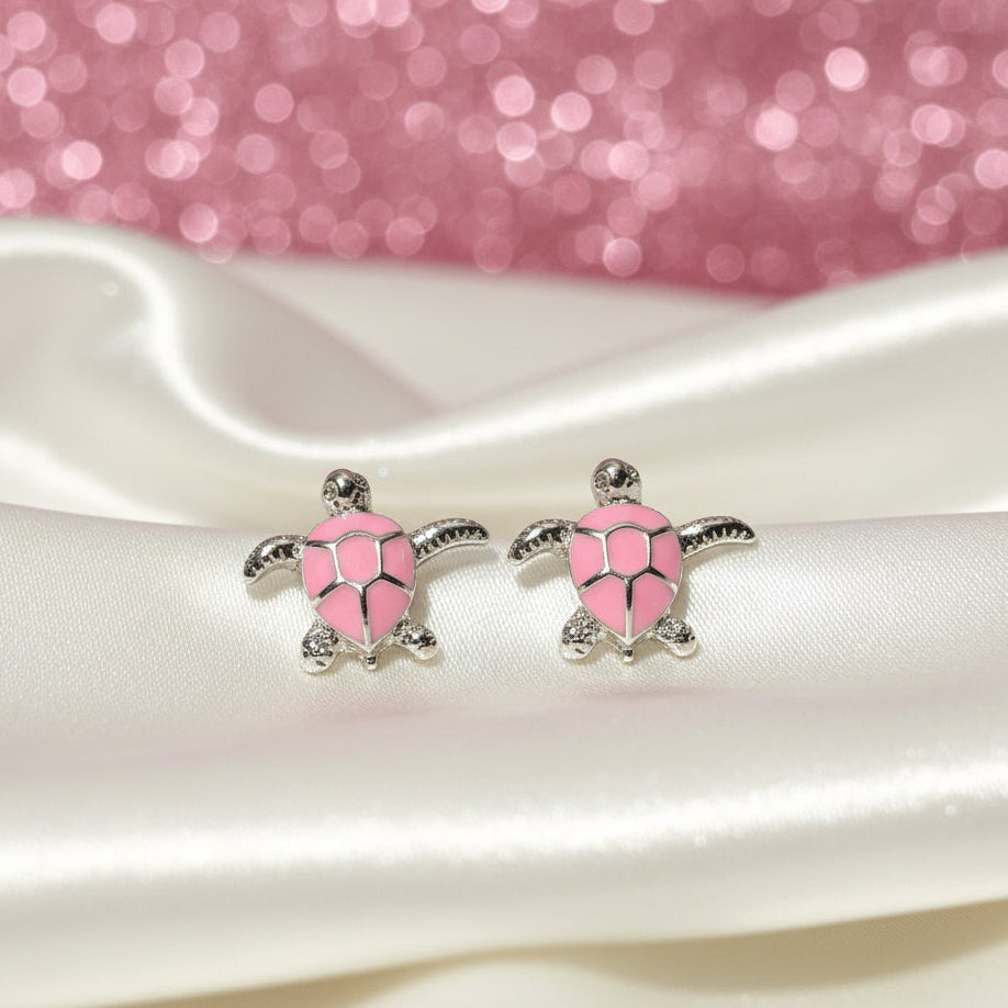 Pink Sea Turtle Earrings on a white satin surface with a pink glittery background