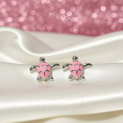 Pink Sea Turtle Earrings on a white satin surface with a pink glittery background