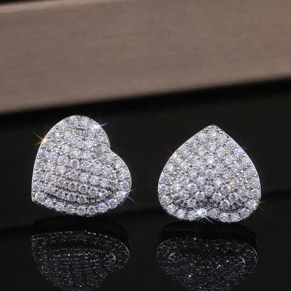 Radiant Heart Pavé Earrings on a reflective black surface with a brown background
