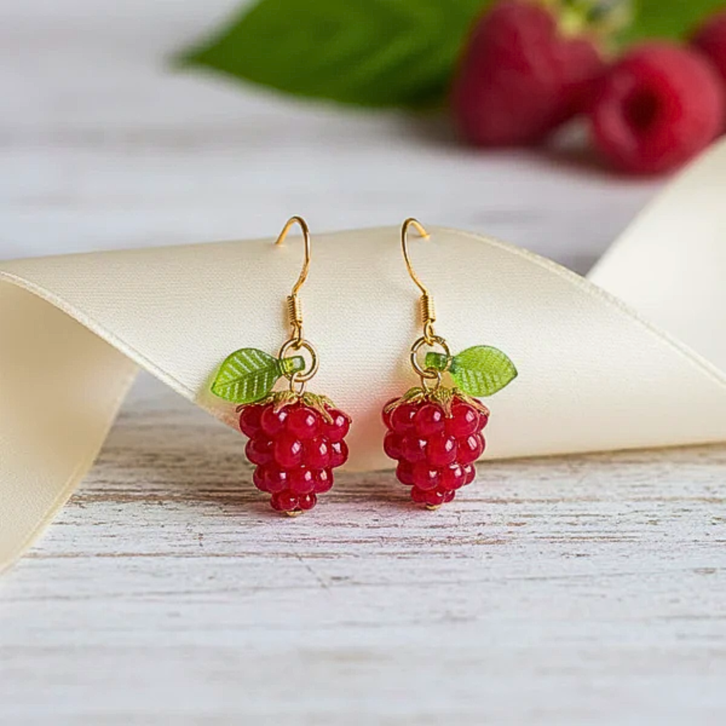Raspberry Drop Earrings with gold hooks on a white ribbon against a light background